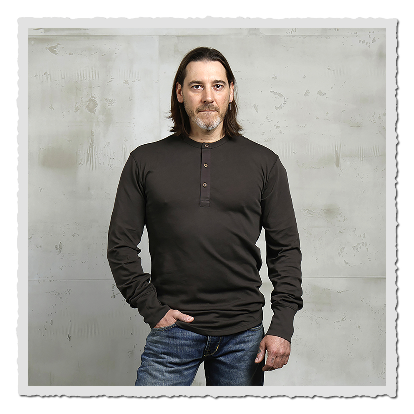 Frontansicht eines Models im braunen Langarmshirt vor heller, strukturierter Wand im Studio.